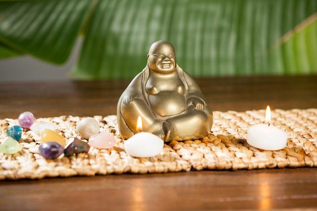 Laughing buddha figurine, pebbles stone and lit candles on mat