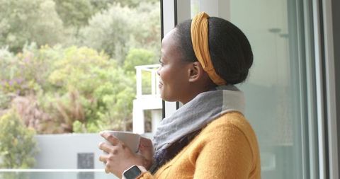 African American Woman Enjoying Morning Coffee on Balcony in Mustard Sweater and Scarf