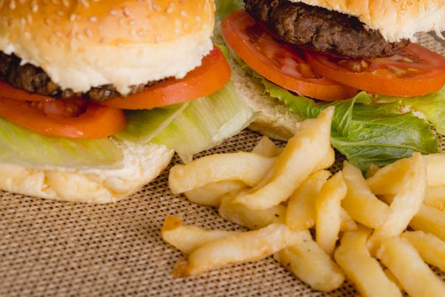 This image showcases a close-up view of a juicy burger with fresh lettuce and tomato, accompanied by crispy french fries on a burlap surface. Perfect for use in advertisements, menus, food blogs, and social media posts promoting fast food, comfort food, or casual dining.