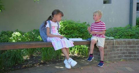 Young students collaborating on homework outside on bench in school courtyard
