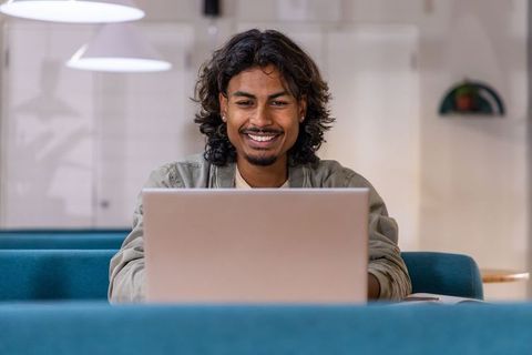 Indian man working on laptop in modern coworking lounge smiling and focused