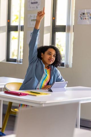 African american girl raising hand in classroom with tablet learning and curious expression