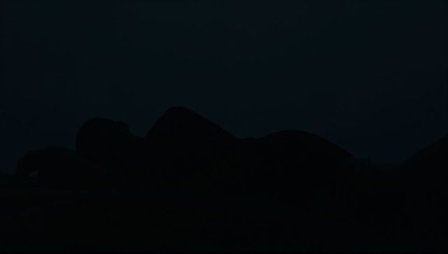 Solitary silhouette lying on bed at night with pillow and blanket, minimal low-light mood