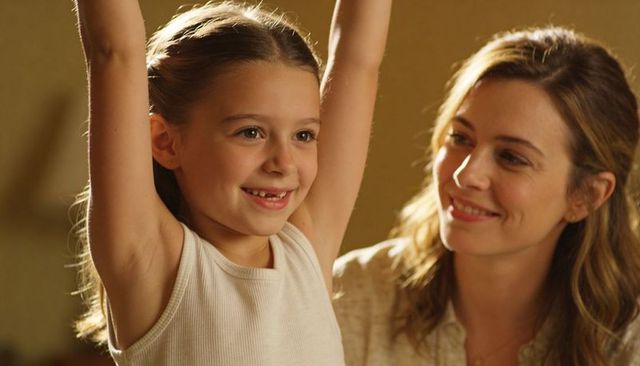 Mother watching daughter raising arms and smiling in warm home sharing tender joyful bond