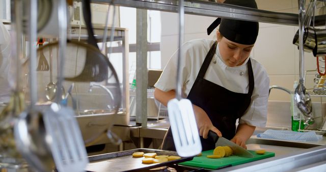 Young chef chopping potatoes on green cutting board in a professional kitchen. Hands-on culinary training and food preparation techniques make this perfect for culinary schools, chef training programs, and cooking workshops. Ideal for illustrating restaurant environments, training material, food blogs, and professional cooking equipment advertisements.