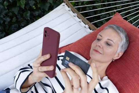 Mature woman relaxing and shopping online from hammock using smartphone with credit card