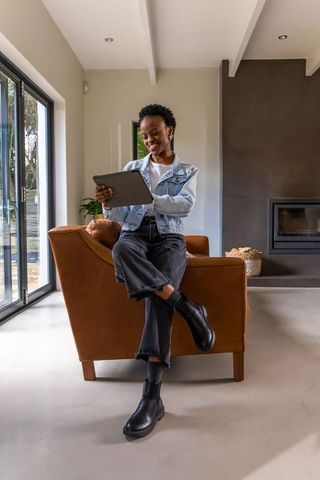 African american woman using tablet while sitting on leather armchair in modern minimalist living ro