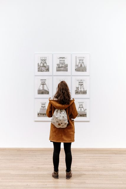 Woman with brown hair enjoying an art exhibit, showcasing multiple framed portraits in a minimalist gallery setting. Perfect for illustrating art appreciation, cultural experiences, or interior decor contexts in modern spaces.
