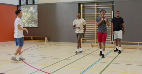 Asian player dribbling past diverse male teammates in indoor gym training session