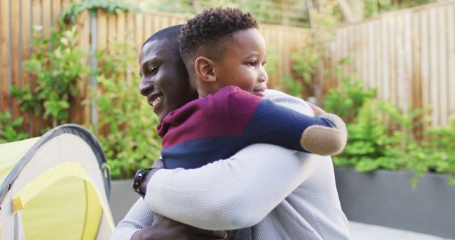 Image of happy african american father and son hugging in garden. Family, spending quality time together at home and garden concept.