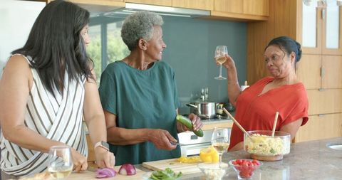 Senior african american women cooking, chopping vegetables and toasting wine in kitchen