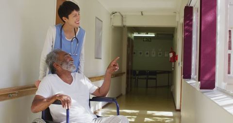 Elderly Man in Wheelchair with Caring Doctor in Retirement Home Corridor