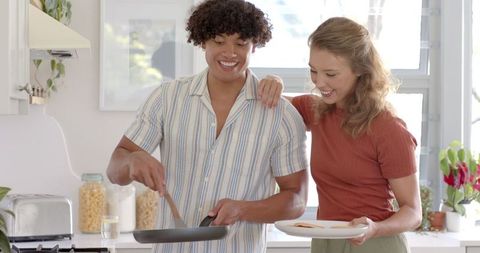 Diverse couple joyfully making breakfast together in modern kitchen