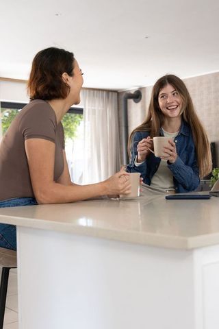 Diverse friends laughing over coffee at kitchen island in bright minimalist home