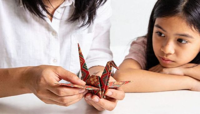 Parent teaching child folding patterned washi origami crane during craft moment