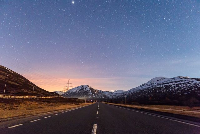 Twilight road with clear starry sky and mountains in the background depicting a tranquil evening scene. This can be used for travel-related content, adventure promotion, inspirational backgrounds or nature enthusiasm.