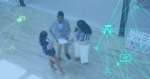Business team collaborating and reviewing tablet in modern atrium with network overlay
