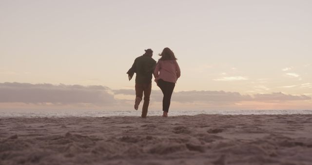 Happy senior caucasian couple holding hands running barefoot on beach at sundown, copy space. Freedom, relationship, retirement, romance, vacations, wellbeing and active senior lifestyle, unaltered.