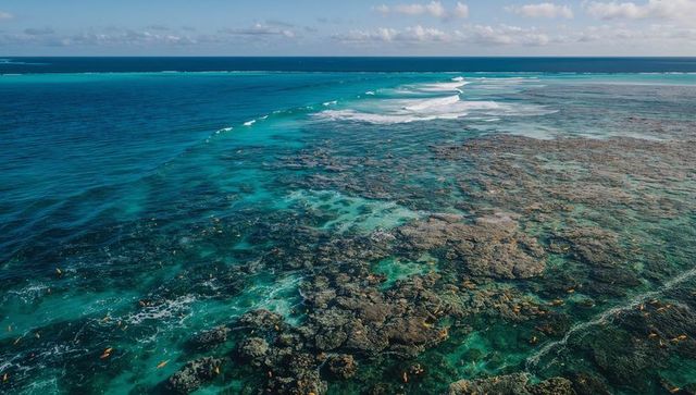 Aerial turquoise coral reef meeting deep ocean with breaking waves and shallow sand flats