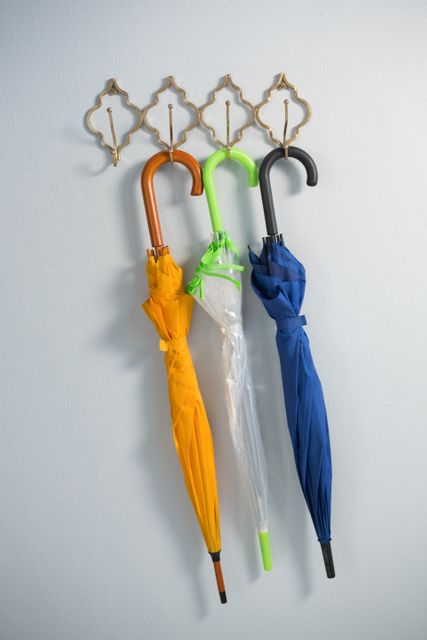 Colorful umbrellas hanging on hook against white wall