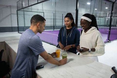 Multicultural group checking in at sports center counter with smoothies and mobile payment