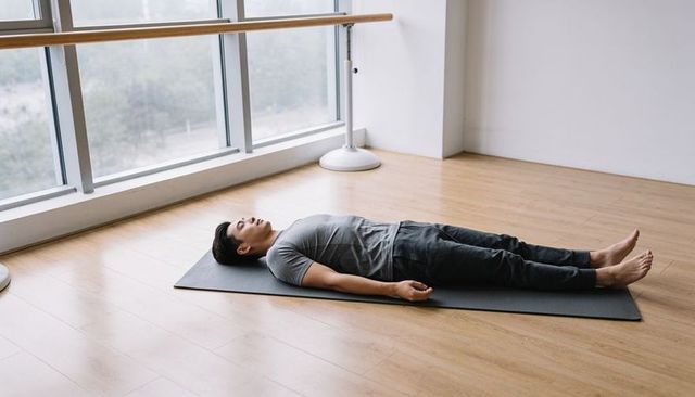 Asian man lying in relaxation pose on yoga mat in bright minimalist studio with barre