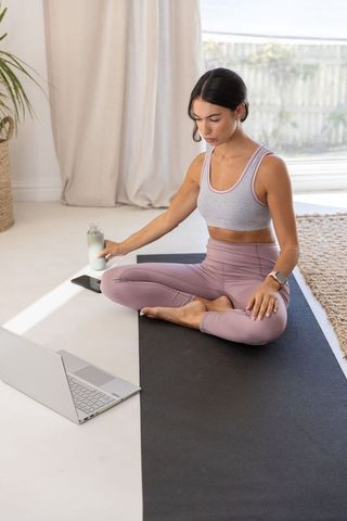 Practicing home yoga on mat, woman grabbing water bottle while following online workout