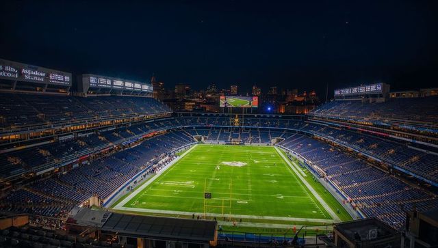 Nighttime aerial view of illuminated american football stadium with city skyline