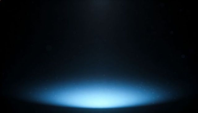 Soft cyan spotlight casting circular glow with dust particles and lens bokeh