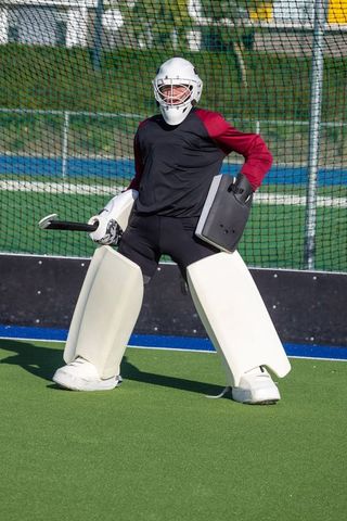 Field hockey goalkeeper in protective gear on turf