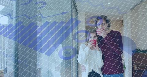 Young couple sipping coffee by glass door with blue financial data overlay in cozy home