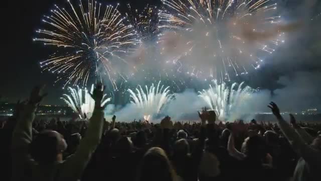 Fireworks Display Over Water with Enthralled Spectators Filming Festive Show