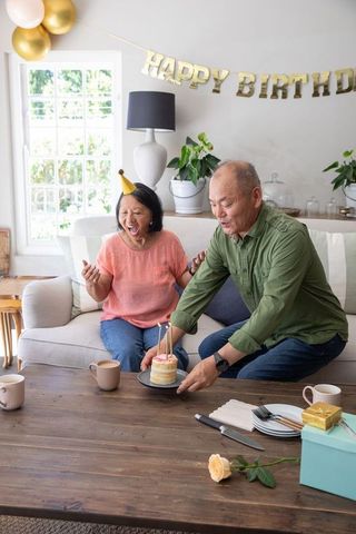 Senior asian couple celebrating intimate birthday at home with mini cake, candles and gifts