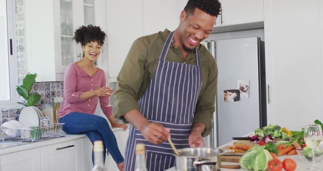 Happy african american couple cooking and drinking wine in kitchen. Spending quality time at home together concept.