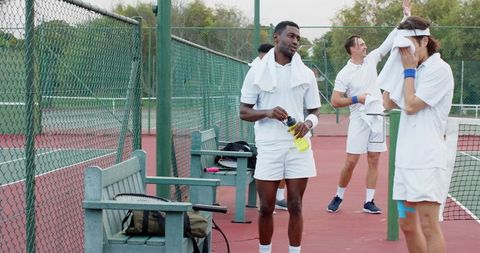 Tennis players resting on outdoor red court holding towels and sports drink