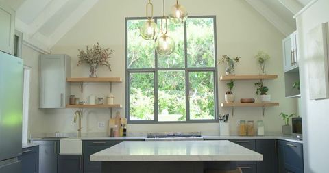 Modern farmhouse kitchen with marble island, black-framed window and brass pendant lights