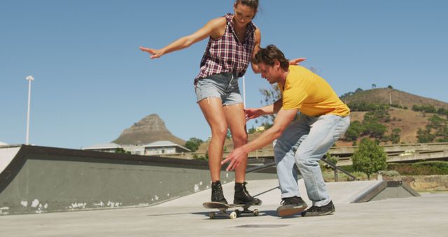 Smiling caucasian man teaching woman how to skateboard on sunny day. hanging out at skatepark in summer.