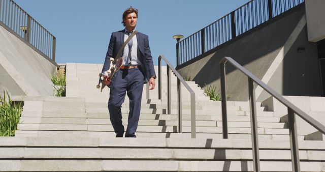 Caucasian businessman walking downstairs, holding skateboard on sunny day. hanging out at skatepark in summer.