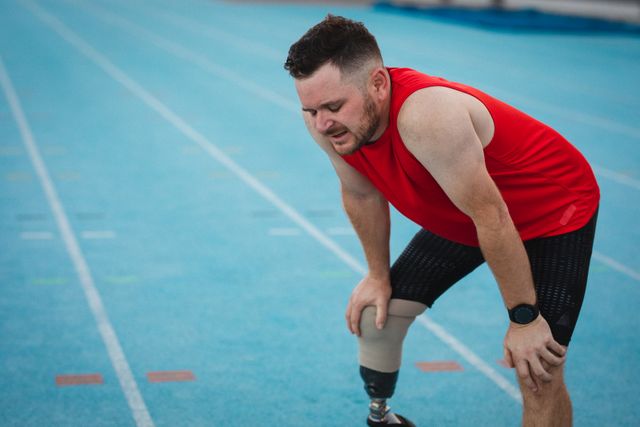 Tired caucasian disabled male athlete with prosthetic leg resting on runway. professional runner training at sports stadium.