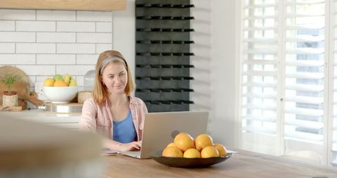Woman Working Remotely in Bright Kitchen with Laptop and Oranges