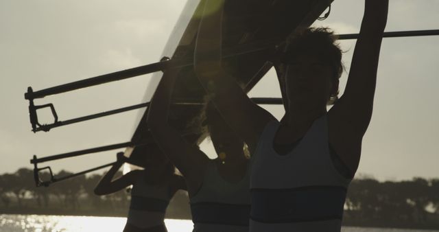 Group of rowers lifting a boat near a lake during sunset. Ideal for use in articles about teamwork, outdoor activities, fitness routines, or rowing sports.