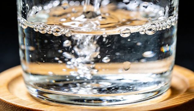 Pouring water forming swirling bubbles in clear glass on wooden coaster