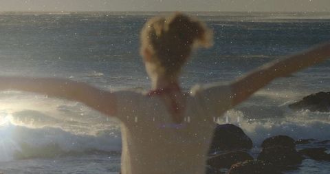 Woman stretching arms toward sunrise over rocky shoreline at golden hour