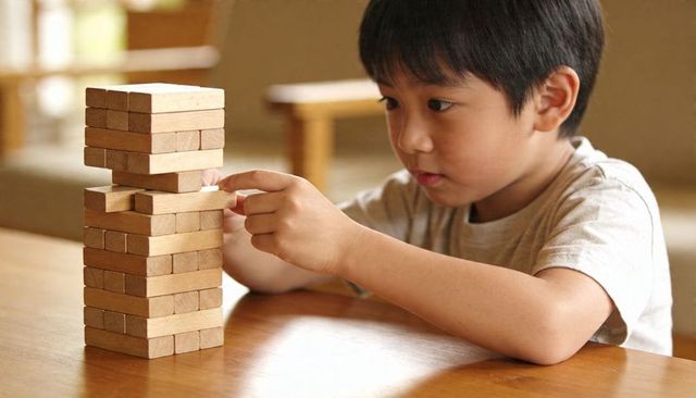 Asian boy concentrating while extracting block from wooden tower playing block-stacking puzzle