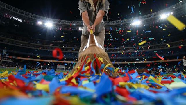 Stadium worker sweeping confetti after celebration under bright floodlights night cleanup