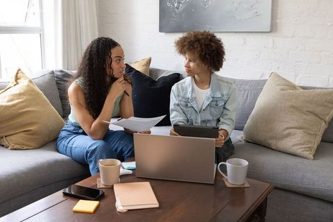 African american women collaborating on laptop and tablet at home discussing notes