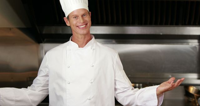Smiling chef standing in a professional kitchen, wearing white uniform and chef hat. Ideal for ads and promotions for restaurants, cooking classes, culinary schools, and food service businesses. Can be used in articles about cooking, chef careers, and hospitality industry. Enhances content related to gastronomy, recipes, and kitchen staff.