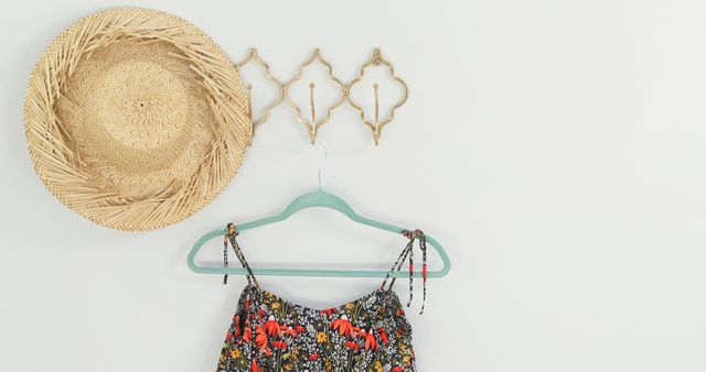 A straw hat and a colorful top hang on a wall, creating a simple and stylish summer vibe, with copy space. The arrangement suggests a carefree, bohemian lifestyle and the joy of sunny days.