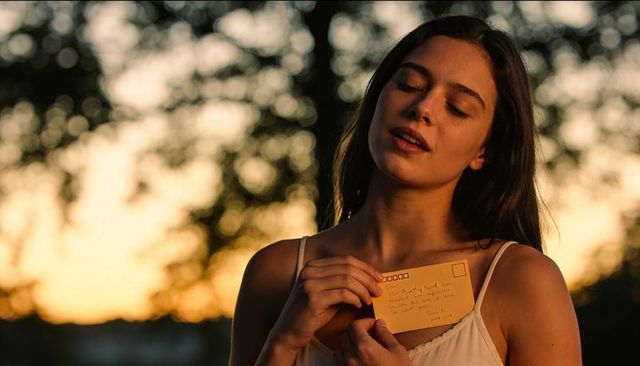 Young woman holding handwritten postcard to chest during golden hour portrait outdoors