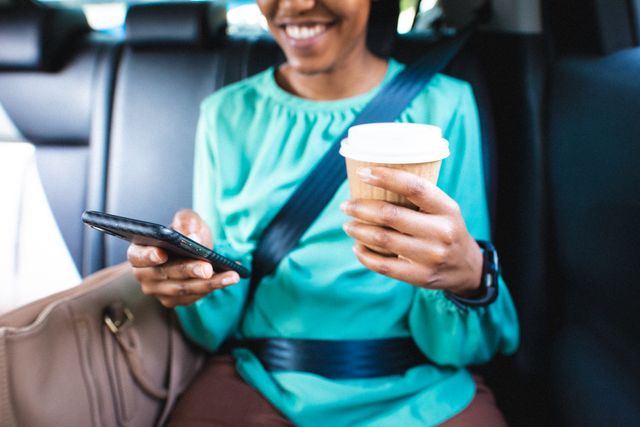 African american mid adult businesswoman with disposable coffee cup using smart phone in car. unaltered, wireless technology, sustainable lifestyle, safety, business person and transportation.